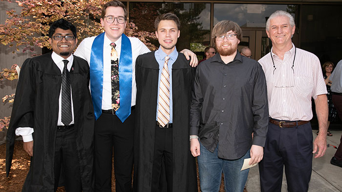 Physics students in graduation regalia pose for a photo with Dr. Mayanovic at a CNAS graduation reception.