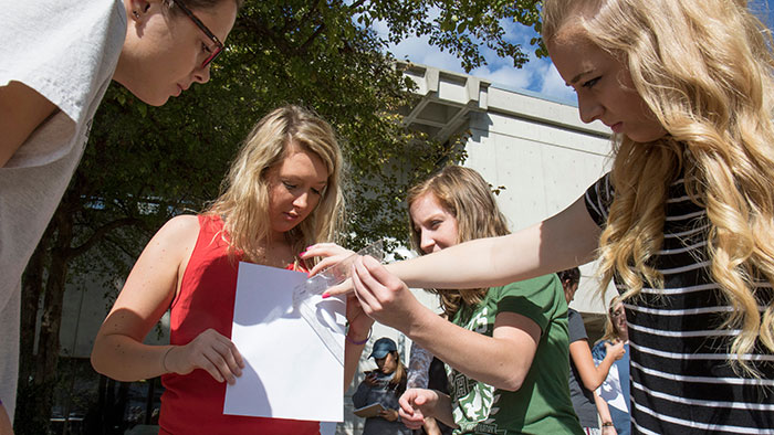 Physics 101 students conduct an outdoor activity with a ruler and paper.